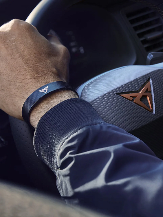 Detailaufnahme eines CUPRA-Lenkrads mit kupferfarbenem Logo, Hand am Steuer mit CUPRA-Armband